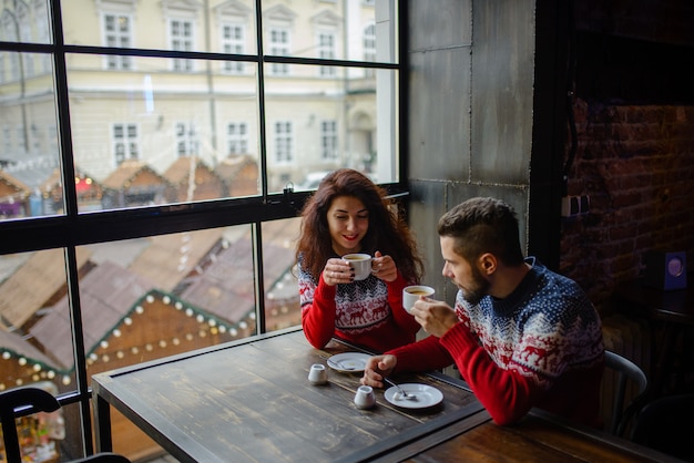 Couple heureux et romantique dans des chandails chauds boit du café dans des gobelets en papier jetables à la cafétéria.