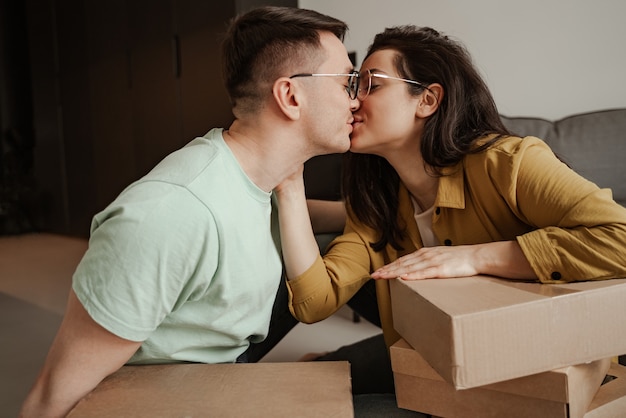 Un couple heureux s'embrasse assis sur de la farine avec des boîtes à la maison. Jeune famille déménageant dans un nouvel appartement.