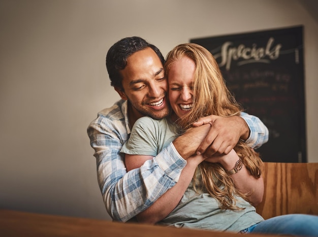 Un couple heureux s'embrasse et sourit pour une étreinte romantique ou un bonheur relationnel au restaurant intérieur