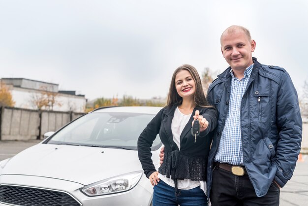 Couple heureux et souriant posant près de la nouvelle voiture