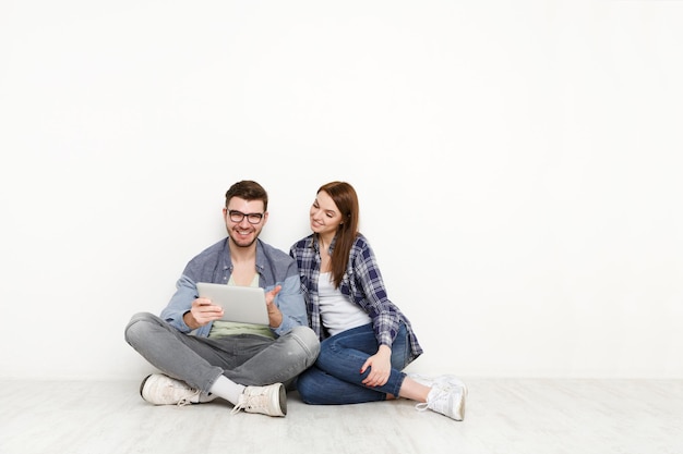 Couple heureux avec tablette, achats en ligne, commande Internet assis à l'étage de la maison dans un salon vide