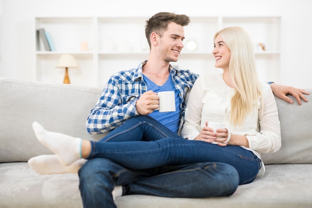 Le couple heureux avec une tasse se détend sur le canapé