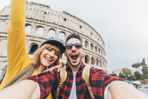 Couple heureux de touristes s'amusant en prenant un selfie devant le Colisée à Rome. Les gens voyagent à Rome, en Italie.