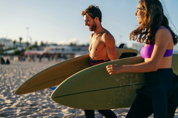 Un couple heureux en vacances marchant sur la plage et faisant du surf