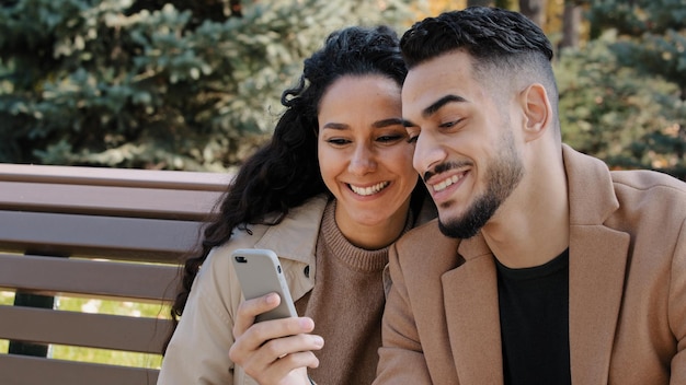 Couple hispanique s'asseoir sur un banc dans le parc d'automne jeune homme tenir le téléphone homme et fille parler regarder l'écran