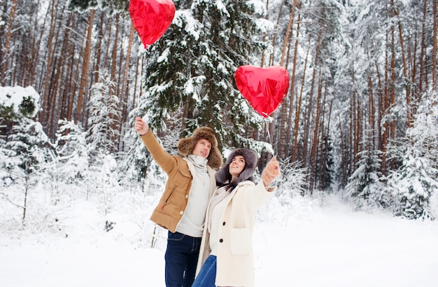 Couple d'hiver amoureux. Garçon et fille étreignant dans la neige d'hiver et la forêt de fées avec des ballons.
