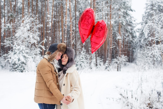 Couple d'hiver amoureux. Garçon et fille étreignant dans la neige d'hiver et la forêt de fées avec des ballons.