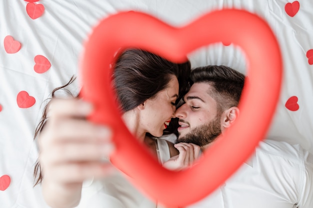 Couple homme et femme amoureux sur lit avec des formes de coeur rouge à la maison