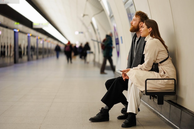 Couple homme et femme assis sur un banc dans une station de métro attendant leur train