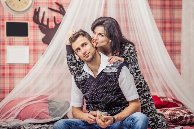 Couple homme et femme dans la chambre à la maison buvant du thé avec des biscuits à l'intérieur de Noël rouge