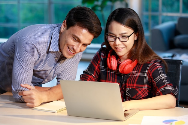 Couple d'hommes et de femmes séjournant ensemble dans le salon au crépuscule du soir et travaillant avec un ordinateur portable, discutant avec des visages heureux. Nouveau concept normal de travail à domicile.