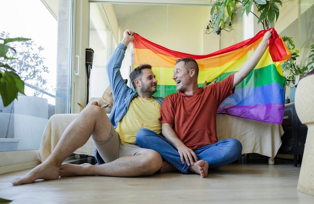 un couple d'homosexuels matures avec un drapeau de fierté gay à la maison