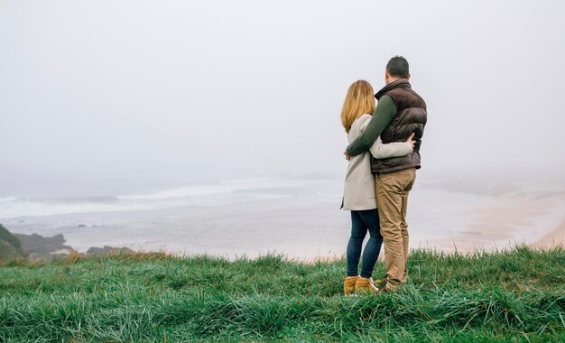 Couple hugging sur la côte par une journée d'hiver brumeuse regardant la vue