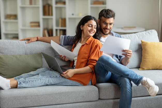 Un couple indien heureux vérifiant des documents, des conjoints lisant un contrat d'assurance ou un certificat de propriété.