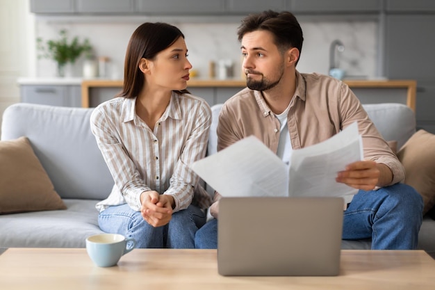 Un couple inquiété examinant des documents avec un ordinateur portable