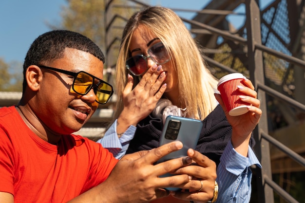Photo un couple interracial heureux vérifiant son téléphone portable à l'extérieur.