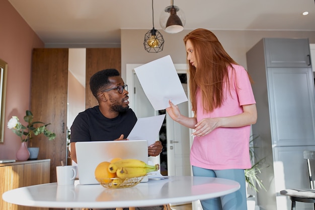 Couple interracial lire le courrier et vérifier la comptabilité dans la cuisine à la maison