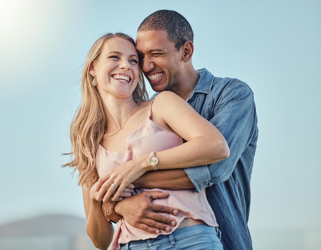 Couple interracial sourire câlin en plein air et heureux ensemble pour des vacances de lune de miel ou un voyage d'été Homme noir embrasse une femme caucasienne avec bonheur comique et amour romance ou liaison au soleil