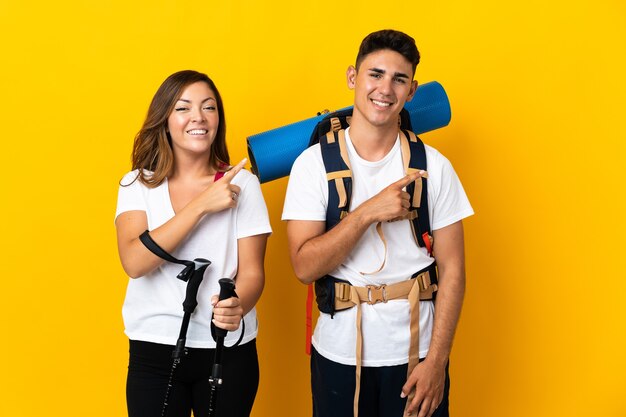 Couple de jeune alpiniste avec un gros sac à dos jaune pointant vers le côté pour présenter un produit