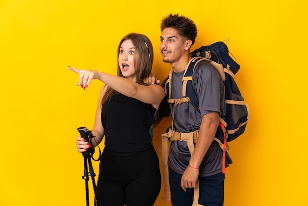 Couple de jeune alpiniste avec un gros sac à dos jaune présentant une idée tout en regardant en souriant vers