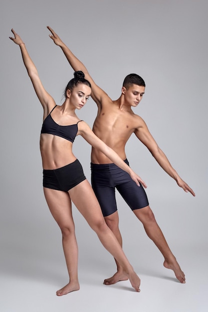 Le couple d'un jeune danseur de ballet moderne en costume noir pose sur un fond de studio gris