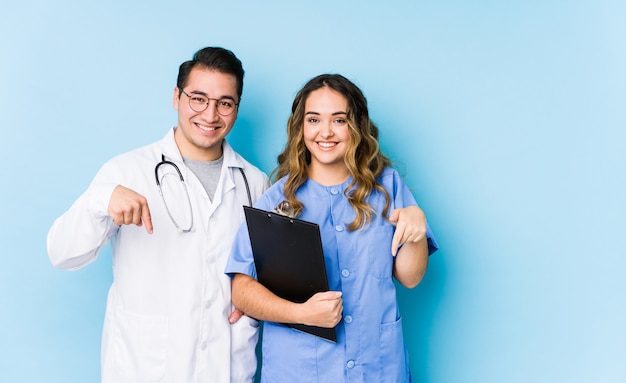 Couple de jeune médecin posant dans un mur bleu isolé pointe vers le bas avec les doigts, sentiment positif.