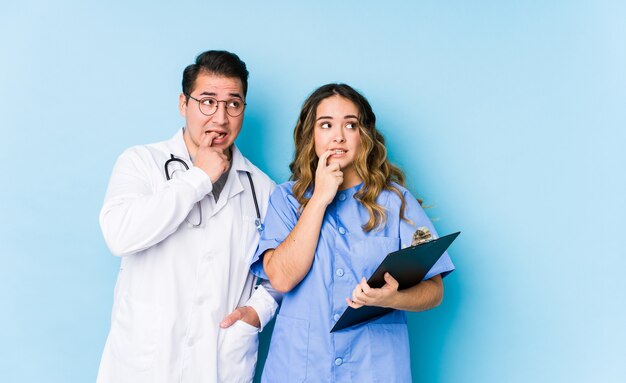 Couple de jeune médecin posant dans une réflexion détendue isolée bleue sur quelque chose en regardant un espace de copie.