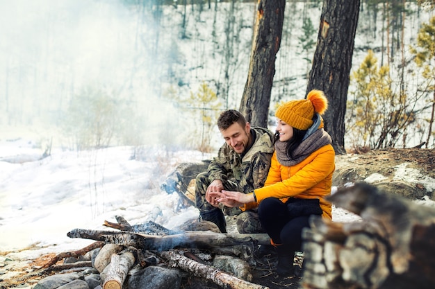 Un couple de jeunes adultes, hommes et femmes, est heureux de s'asseoir ensemble en hiver autour du feu de camp