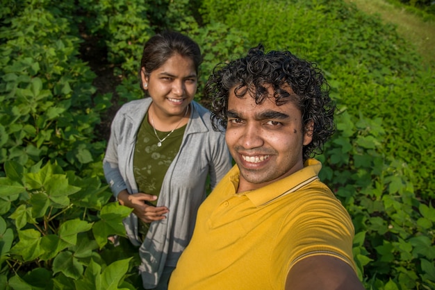 Couple de jeunes agriculteurs prenant un selfie avec un smartphone ou un appareil photo dans la ferme de coton.