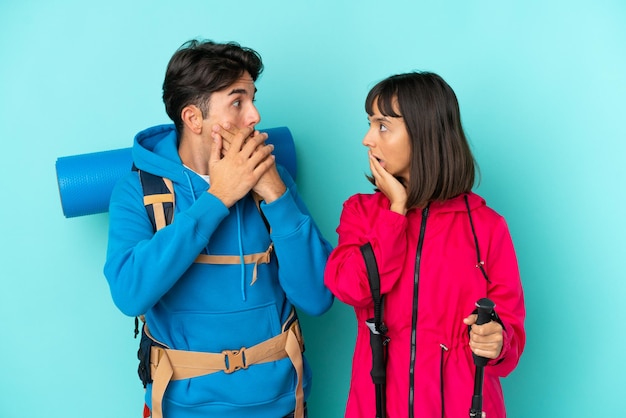 Couple de jeunes alpinistes isolé sur fond bleu couvrant la bouche avec les mains pour dire quelque chose d'inapproprié