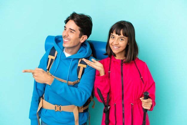 Couple de jeunes alpinistes isolé sur fond bleu pointant vers l'arrière et présentant un produit
