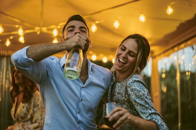 Couple de jeunes amis s'amusant à boire lors d'une fête - des gens ivres dansent ensemble