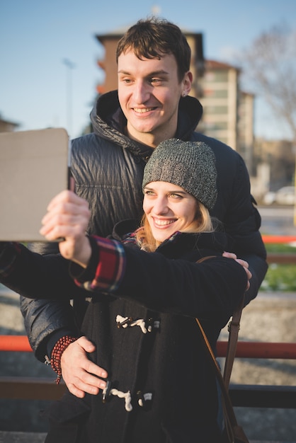 Un couple de jeunes amoureux assis sur le trottoir, s&#39;amuser tout en utilisant la tablette internet connecté ville