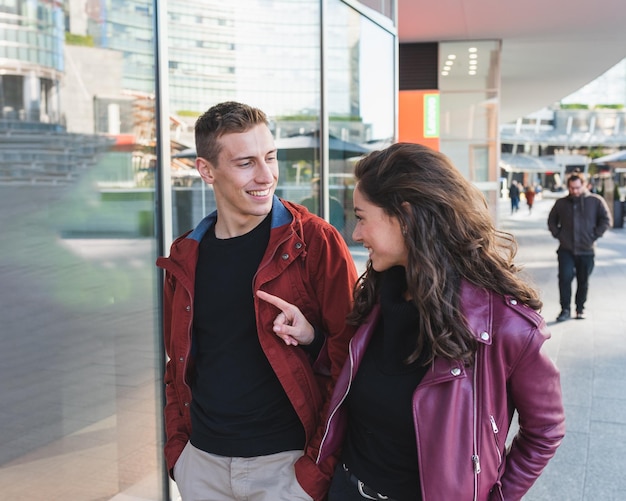 Un couple de jeunes amoureux se promène dans la ville en faisant du shopping, elle indique ce qu'elle aimerait comme cadeau, il a l'air heureux Concept d'amour Shopping pour les cadeaux de la Saint-Valentin