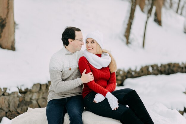 Un couple de jeunes amoureux en vestes et foulards d'hiver assis dans un parc à neige