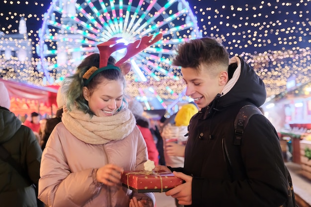 Couple de jeunes au marché de Noël. Joyeuses fêtes garçon et fille donnant une boîte-cadeau