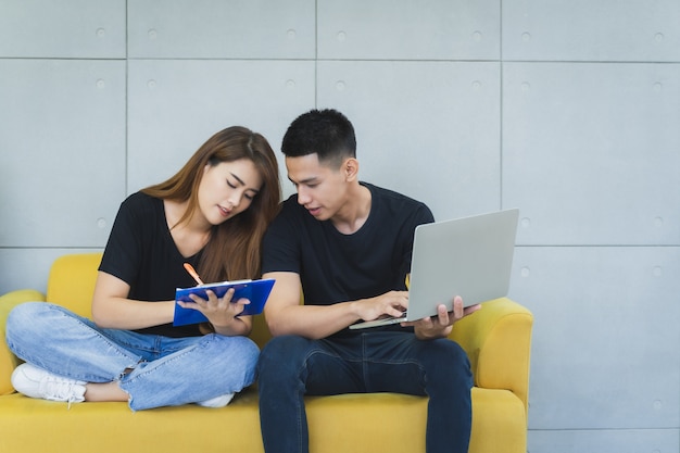 Un couple de jeunes entrepreneurs asiatiques heureux sme en vêtements décontractés au visage souriant utilise un ordinateur portable et vérifie le produit en stock et écrit dans le presse-papiers au bureau à domicile de leur startup, vendeur-livreur