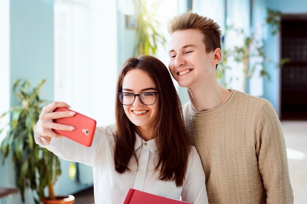 Couple de jeunes étudiants joyeux faisant selfie sur un téléphone mobile rouge