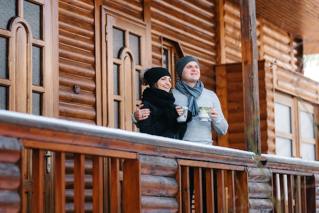 Couple de jeunes un gars et une femme sur le porche d'une maison en bois couverte de neige dans les montagnes d'hiver