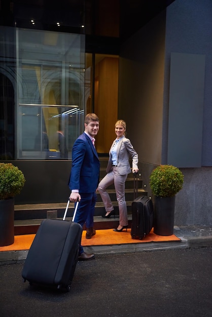 Couple de jeunes gens d'affaires entrant dans l'hôtel de la ville, à la recherche d'une chambre, tenant des valises en marchant dans la rue