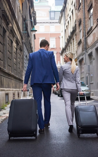 Couple de jeunes gens d'affaires entrant dans l'hôtel de la ville, à la recherche d'une chambre, tenant des valises en marchant dans la rue