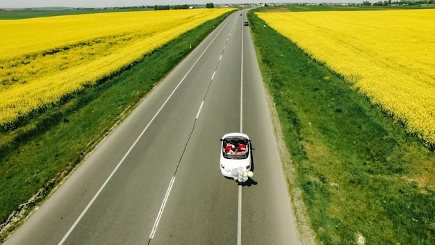 Un couple de jeunes mariés conduit une voiture rétro décapotable sur une route droite de campagne pour leur lune de miel