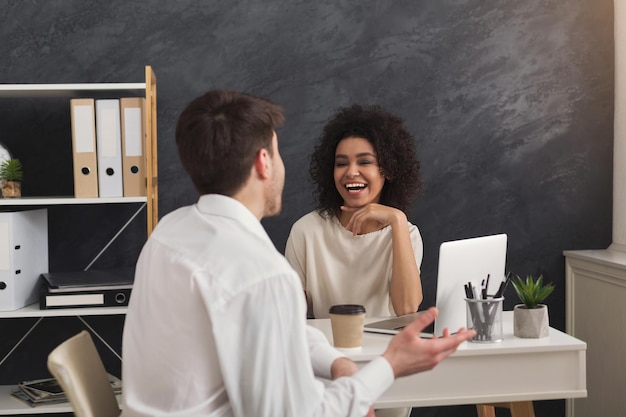 Couple de jeunes partenaires commerciaux heureux travaillant dans un bureau moderne. Femme souriante discutant d'un nouveau projet avec son collègue en buvant du café, espace de copie