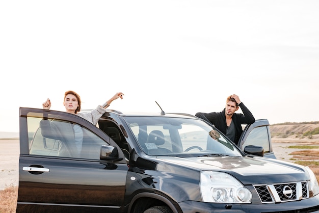 Couple de jeunes voyageurs debout près de la voiture à l'extérieur sur le terrain