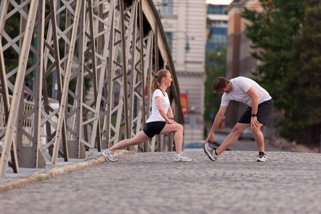 couple de jogging s'échauffant et s'étirant avant l'entraînement de course à pied du matin dans la ville avec le lever du soleil en arrière-plan