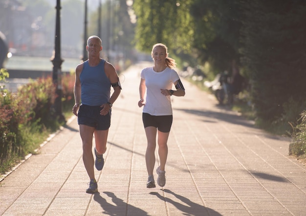 couple de jogging s'échauffant et s'étirant avant l'entraînement de course à pied du matin dans la ville avec le lever du soleil en arrière-plan