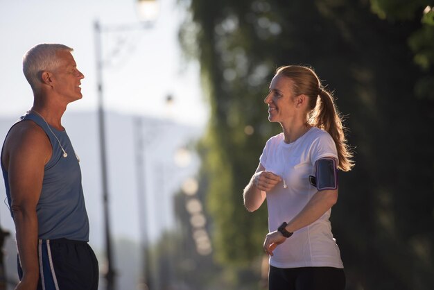 couple de jogging vérifier la liste de lecture de musique sur le téléphone et planifier l'itinéraire avant l'entraînement de course du matin avec le lever du soleil dans la ville et l'éruption du soleil en arrière-plan