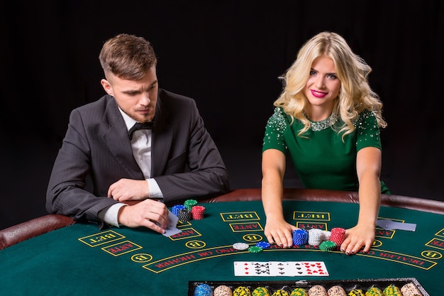 Couple jouant au poker à la table verte. La fille blonde et un gars en costume. jetons de paris all-in