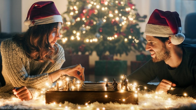 Un couple joue aux échecs à Noël sur un tapis blanc.