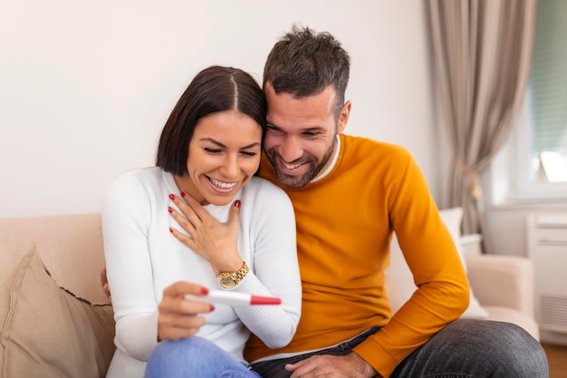 Couple joyeux découvrant les résultats d'un test de grossesse à la maison Couple heureux regardant un test de grossesse Femme surprenant son mari avec un test de grossesse positif, il semble raisonnablement satisfait